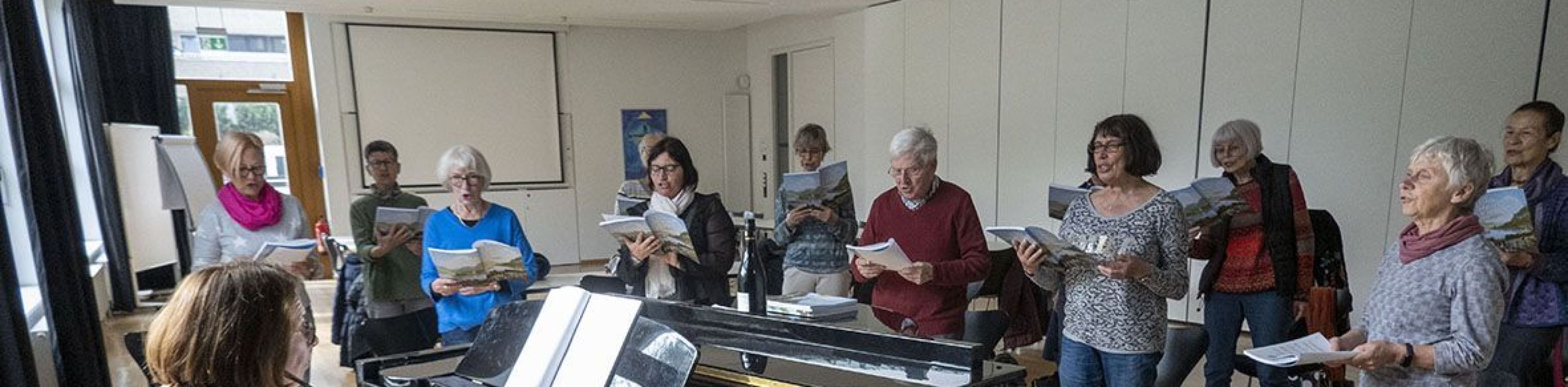 Eine Gruppe &auml;lterer Damen und Herren steht neben einem Piano und singt zu Musikbegleitung., &copy; keb Heilbronn e.V.