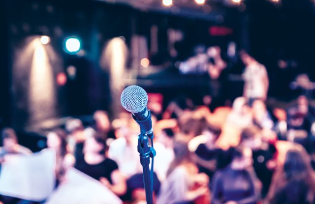 Blick von einer B&uuml;hne &uuml;ber ein Mikrophon im Vordergrund  in einen vollen Zuschauerraum, &copy; HHN